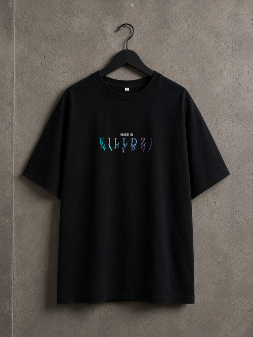 T-shirt oversize noir Made in Killdzi avec logo brodé multicolore, suspendu sur cintre sur fond béton industriel.