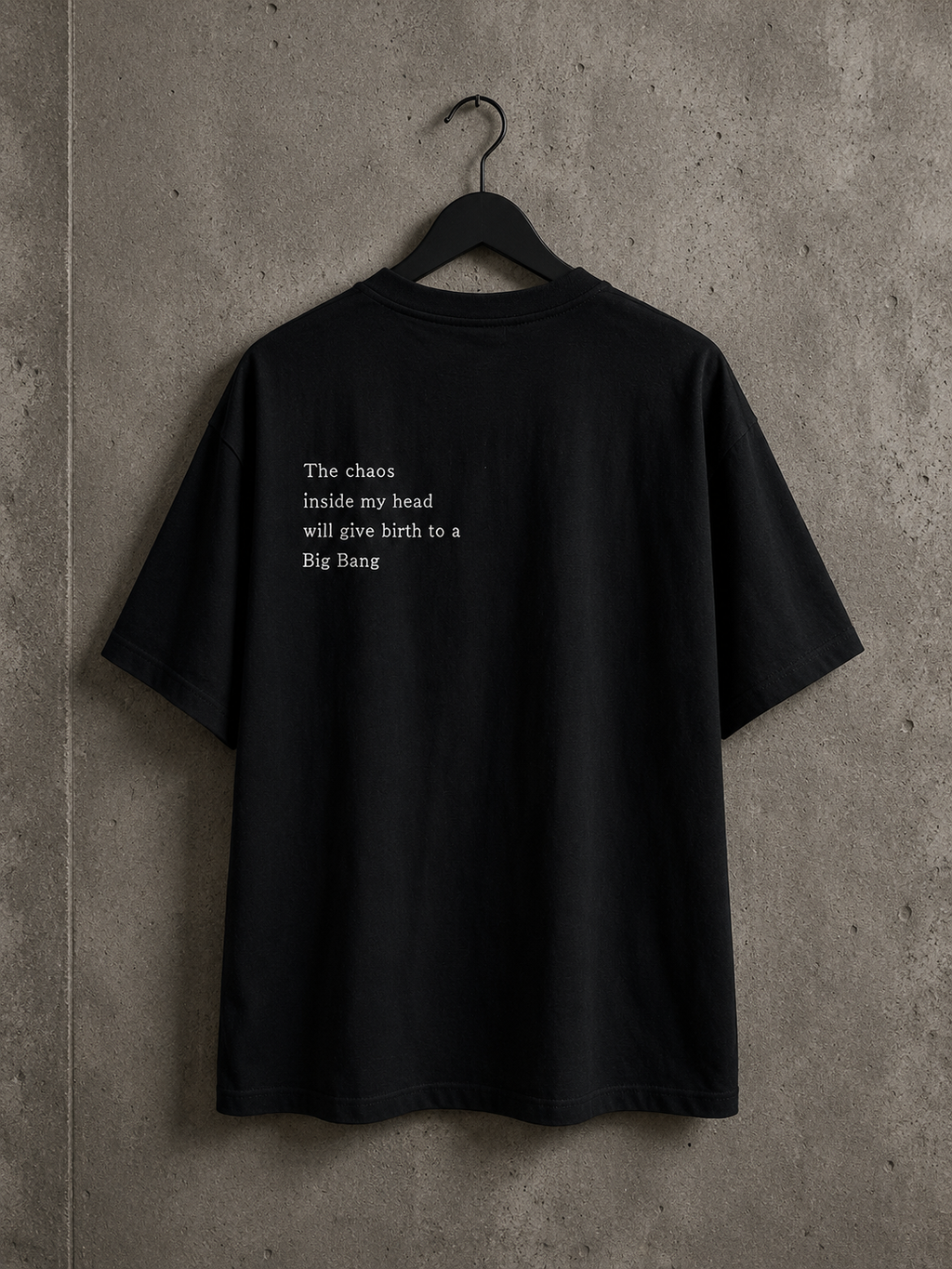 Vue arrière du t-shirt oversize noir Made in Killdzi avec citation brodée à la main, présenté sur cintre devant un mur en béton