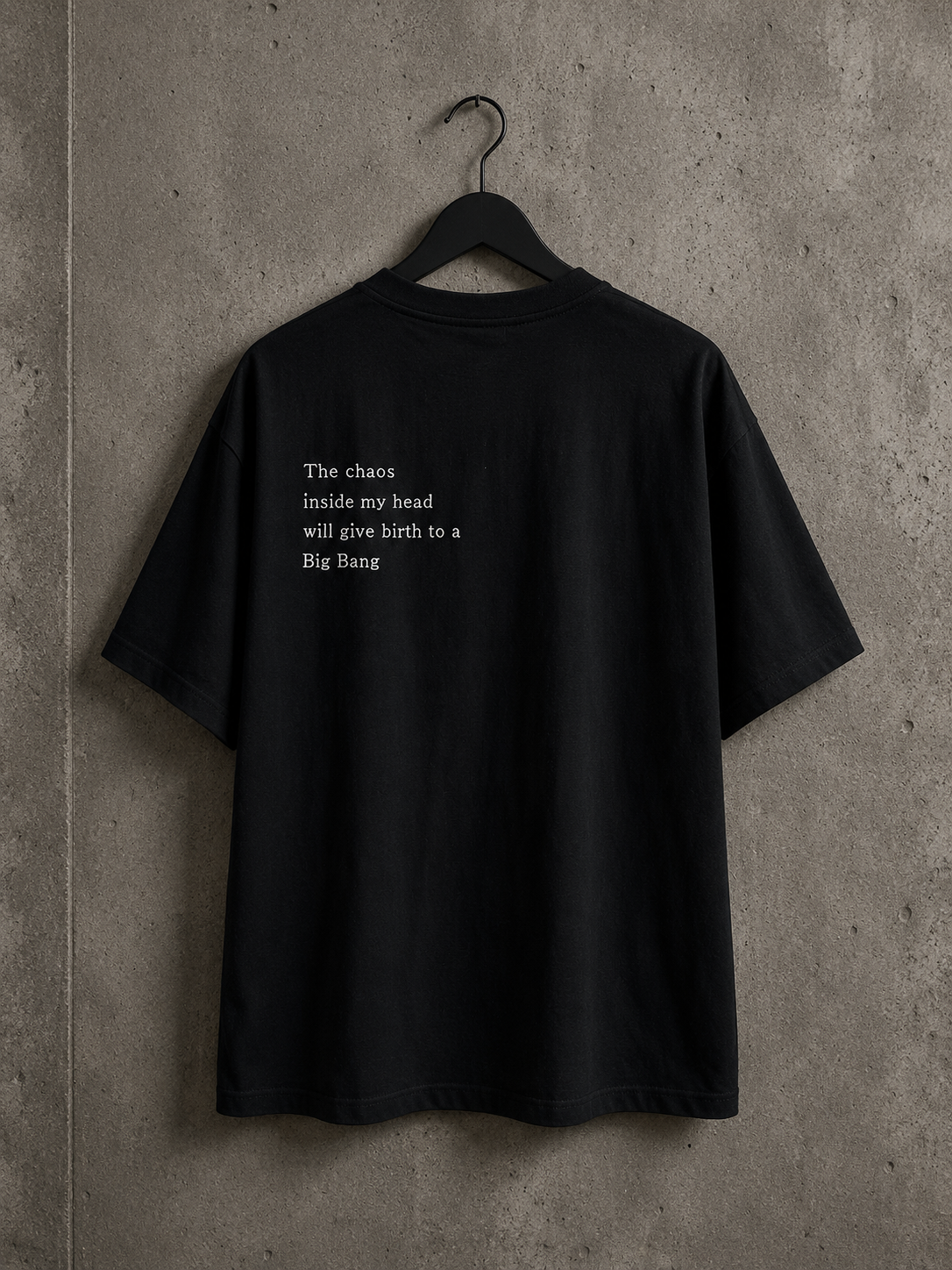 Vue arrière du t-shirt oversize noir Made in Killdzi avec citation brodée à la main, présenté sur cintre devant un mur en béton